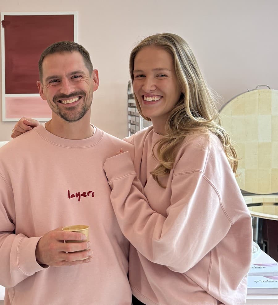 Marian und Sophia, die Gründer:innen von Kreativbrücke e.V., lachend in ihren pinken layers-Pullovern